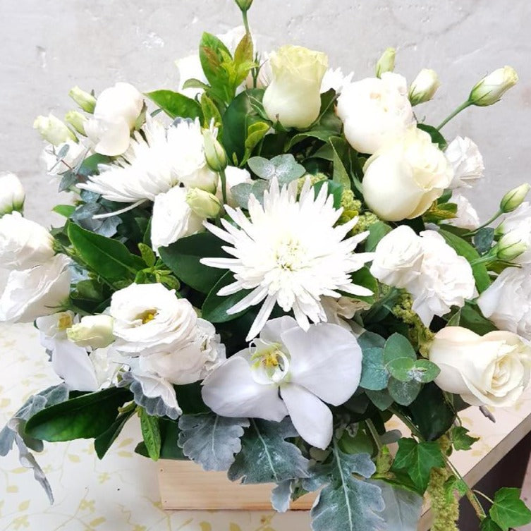 A white and green flower arrangement in a box with Roses, Lisianthus and Phalaenopsis chrysanthemums