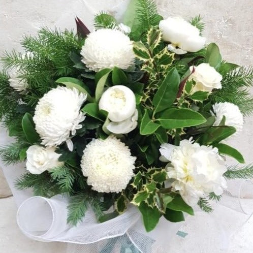 White and green Christmas bouquet with beautifully arranged statement flowers of Big Mama chrysanthemums, Colombian roses and peonies, made all the more festive nestled is spruce and holly. It's wrapped in a white fine mesh.